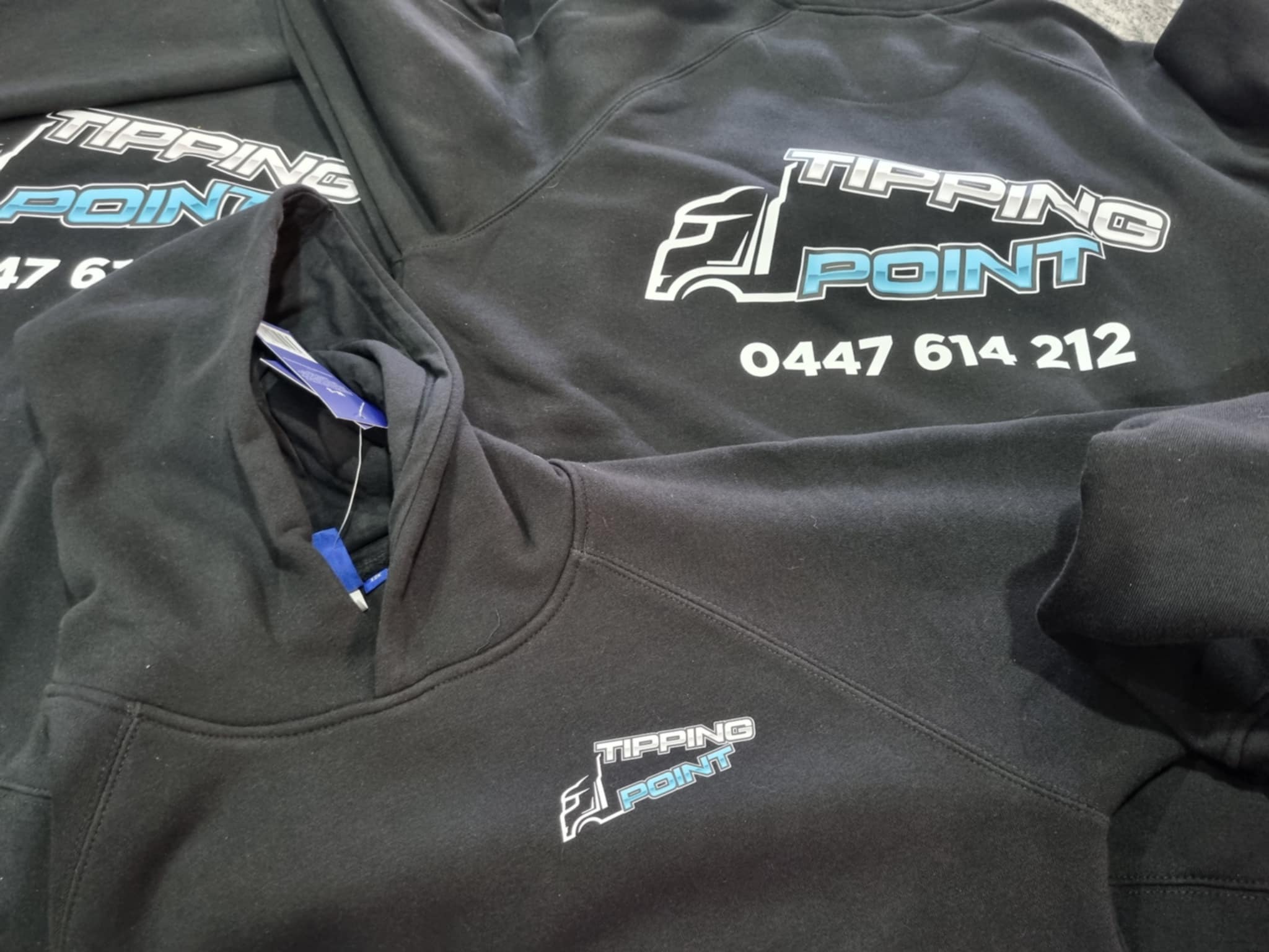 Black hoodies with 'Tipping Point' logo and contact information on a flat surface.