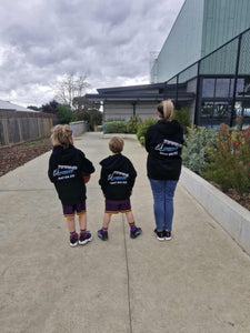 Three people wearing matching black jackets with logos, walking on a sidewalk.