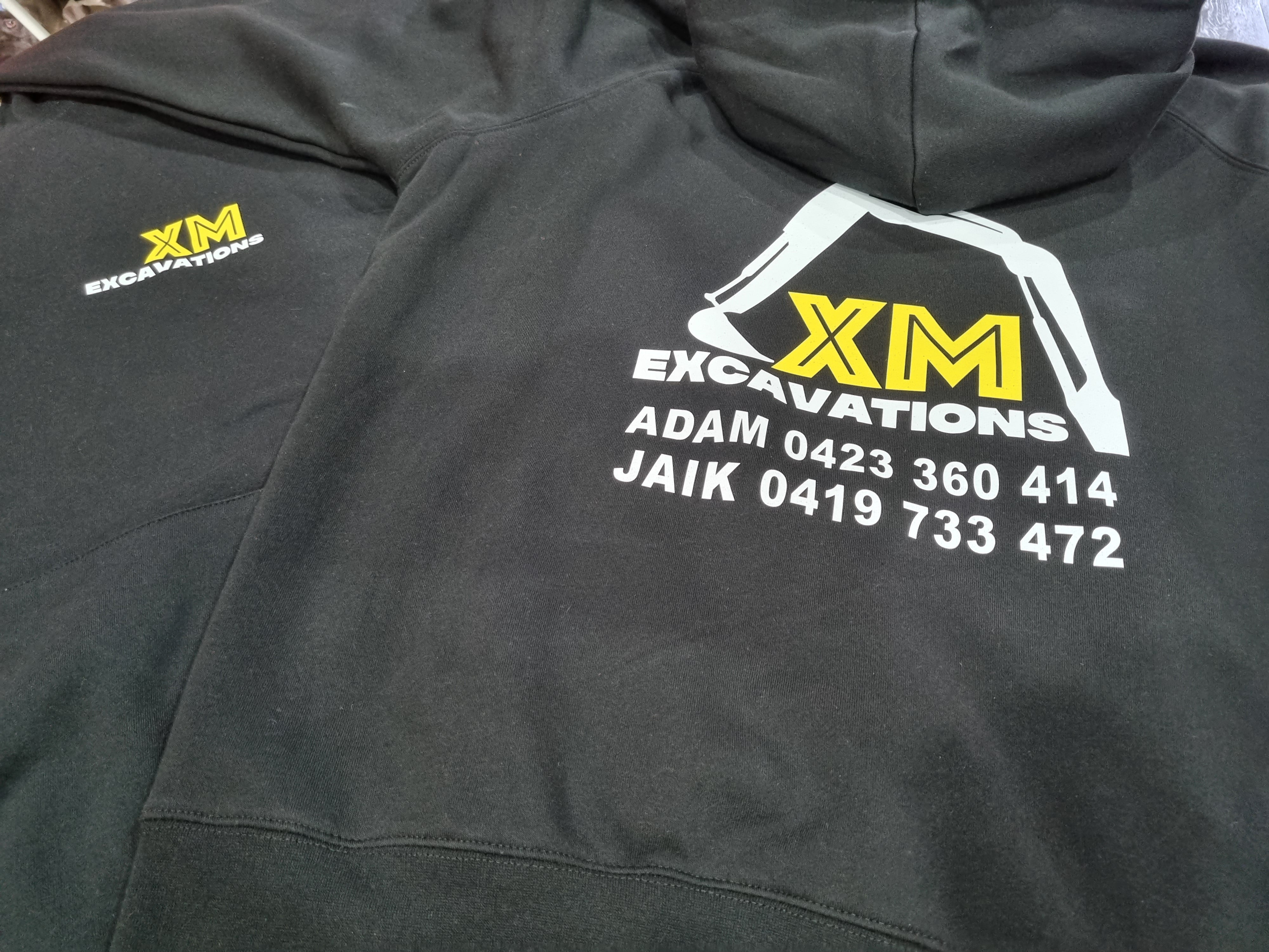 Black hoodie with XM Excavations logo and contact information on a flat surface